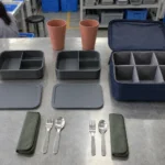Two divided boxes two tumblers two stainless utensil pairs and partitioned case — AI-generated conceptual illustration